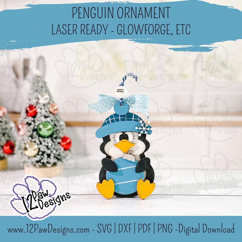 Pode incluir: Um enfeite de pinguim azul e branco com um chap&eacute;u azul e um floco de neve. O enfeite est&aacute; segurando uma bola azul e branca listrada. O enfeite est&aacute; pronto para laser para Glowforge, etc. O texto "2022" est&aacute; no enfeite.