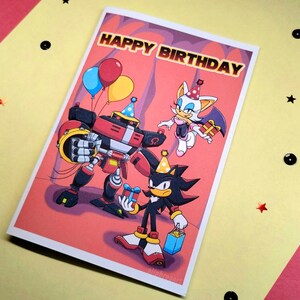 Sonic birthday card laying on table that says Happy Birthday at the top in a colorful Sonic themed font. Image has Team Dark (Shadow, Rouge, and Omega) holding gifts.