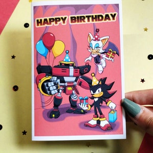 Sonic birthday card being held in hand that says Happy Birthday at the top in a colorful Sonic themed font. Image has Team Dark (Shadow, Rouge, and Omega) holding gifts.