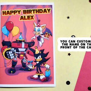Personalized sonic birthday card laying on table that says Happy Birthday at the top in a colorful Sonic themed font. Image has Team Dark (Shadow, Rouge, and Omega) holding gifts.