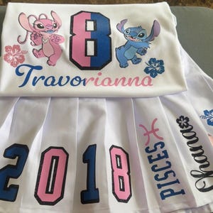 May include: A white t-shirt and a white pleated skirt set featuring blue and pink graphics of Stitch and Angel characters. The shirt displays the number 8 and the name Travorianna. The skirt features the number 2018, the word Ohana, and Pisces text.