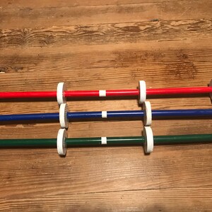 May include: Three wooden dowels with white end caps, painted red, blue, and green. Each dowel has a white stripe in the center.