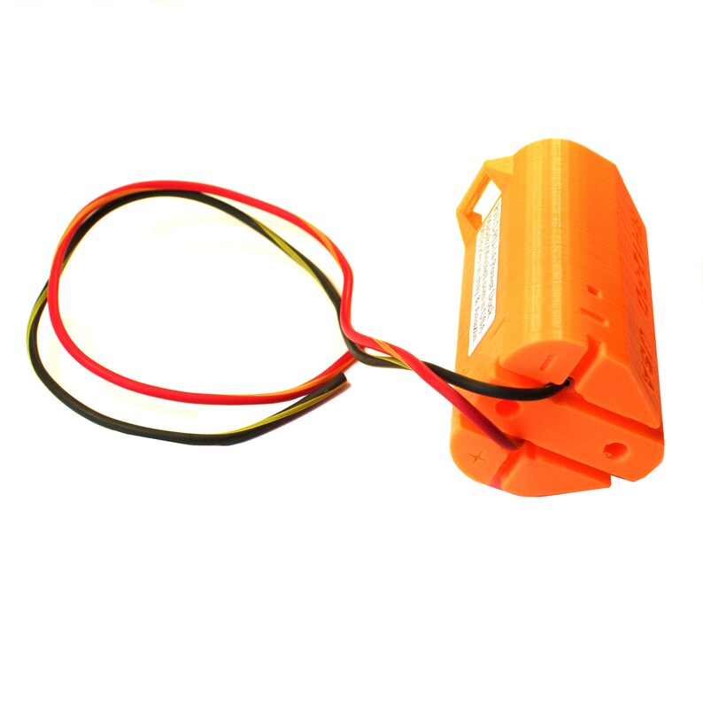 Puede incluir: Un soporte de bater&iacute;a impreso en 3D de color naranja con tres cables conectados. Los cables son negro, rojo y amarillo. El soporte de bater&iacute;a tiene un signo m&aacute;s y un signo menos en el lateral.