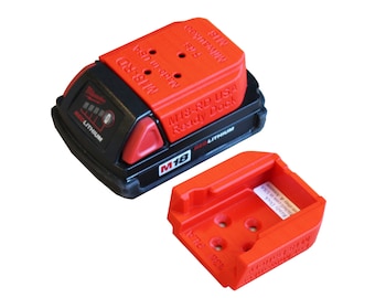 May include: A red and black Milwaukee M18-RD USA Ready Dock for charging and storing batteries. The dock has a red base and a black top with the text "M18-RD USA Ready Dock" printed on it. The dock is designed to fit Milwaukee M18 batteries.