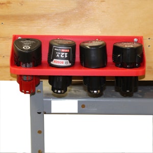 May include: Red plastic wall mount organizer for holding four power tool batteries. The organizer has four slots and is mounted on a wooden surface. The batteries are labeled "Bosch 12V Max 2.0 Ah Li-Ion".