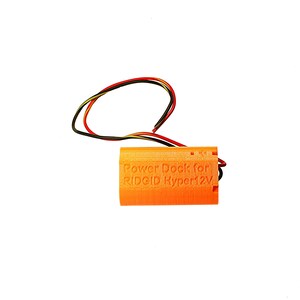 Puede incluir: Base de alimentaci&oacute;n naranja impresa en 3D para una herramienta RIDGID Hyper 12V. La base tiene cables negros y rojos.