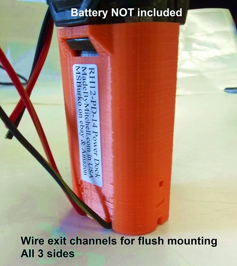 Puede incluir: Un soporte de bater&iacute;a naranja impreso en 3D con una etiqueta que dice "RH12-PD-14 Power Dock Made By Mitchell.com in USA MSBurko on ebay & Amazon". El soporte tiene canales de salida de cables en los tres lados para una instalaci&oacute;n empotrada.