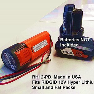 Puede incluir: Primer plano de dos bater&iacute;as de herramientas el&eacute;ctricas de color naranja y azul. La bater&iacute;a naranja est&aacute; etiquetada con "RH12-PD-14 Power Dock MadeByMitchell.com in USA MSBurko on ebay & Amazon". La bater&iacute;a azul est&aacute; etiquetada con "RIDGID 12V High Capacity" y tiene el texto "Batteries NOT included". El texto "RH12-PD, Made in USA Fits RIDGID 12V Hyper Lithium. Small and Fat Packs" est&aacute; escrito debajo de las bater&iacute;as.