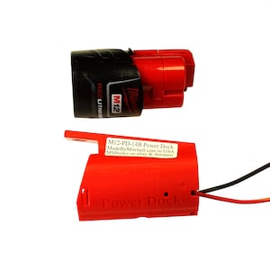 Puede incluir: Un muelle de alimentación Milwaukee M12 rojo y negro con una etiqueta que dice "M12-PD-14B Power Dock MadeByMitchell.com in USA MSBurko en ebay & Amazon".