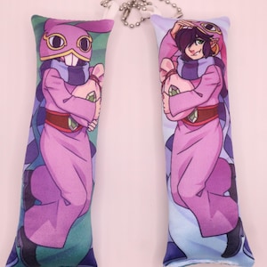May include: Two long, rectangular plush keychains featuring anime-style characters. One has a purple mask and a toothy grin, the other has a similar design. Both have pink robes, brown belts, and green gems. They are connected by a silver chain.