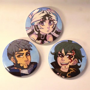May include: Three round button pins featuring cartoon characters. The first pin features a white-haired character with blue eyes and a white feathered headband. The second pin features a character with brown hair and a beard. The third pin features a character with green hair and a red scar on their face.
