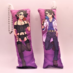 May include: Two purple pillow keychains with different images printed on them. One keychain features a person in a black lace outfit holding a red rose. The other keychain features a person in a white lab coat holding a blue rose.