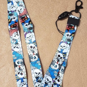 May include: A blue and white lanyard with a repeating pattern of cartoon characters. The lanyard has a black clip and a black breakaway clasp.