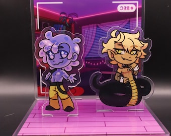 May include: A clear acrylic display featuring two cartoon characters. One is a blue figure in yellow pants, the other a blonde figure with a snake tail. The background is a pink room with a neon sign and the word "REC".