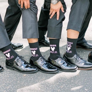 May include: A group of men wearing black dress shoes and black socks with a Mickey Mouse design and the date 04.17.21. The socks say "Groom", "Best Man", and "Father of the Groom".