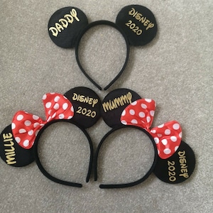 May include: Three black headband mouse ears with red and white polka dot bows. The ears are personalized with the text "Daddy", "Mummy", and "Millie". The text "Disney 2020" is on two of the ears.