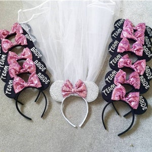 Op de afbeelding: Set van zwarte hoofdbanden met roze paillettenbogen en witte tule sluiers. Sommige hoofdbanden zeggen "Bride" en andere zeggen "Team Bride".