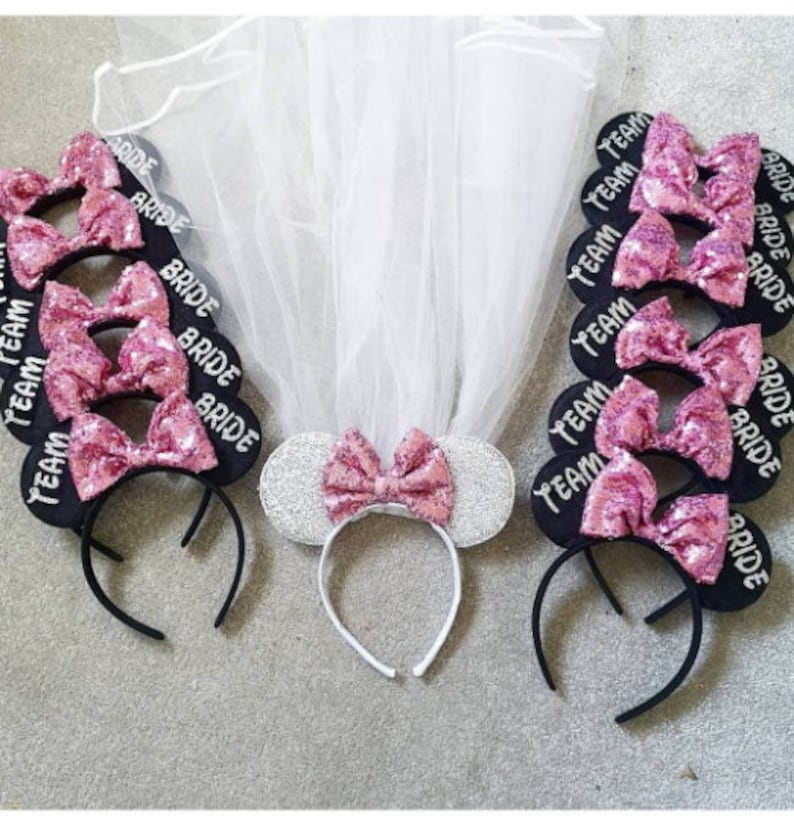 Op de afbeelding: Set van zwarte hoofdbanden met roze paillettenbogen en witte tule sluiers. Sommige hoofdbanden zeggen "Bride" en andere zeggen "Team Bride".