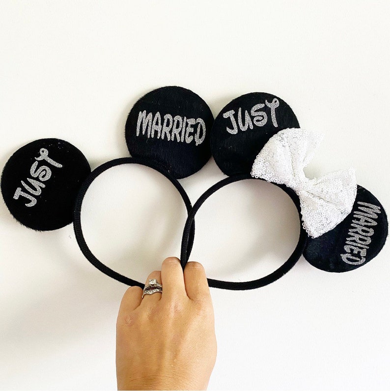 Puede incluir: Orejas de rat&oacute;n negras con letras plateadas brillantes que dicen "Just Married" y "Married". Las orejas est&aacute;n unidas a una diadema negra.