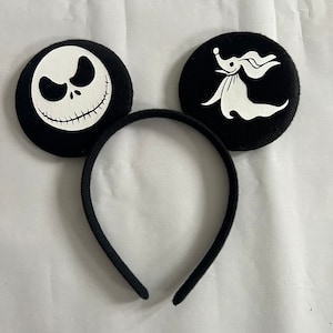May include: Black headband with two black felt circles. One circle features a white Jack Skellington face and the other circle features a white Zero the Ghost Dog.