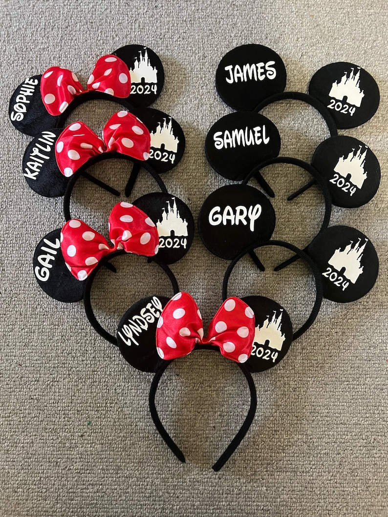 May include: Set of six black mouse ears with red and white polka dot bows. Each ear has a white silhouette of Cinderella's castle and the year 2024. The ears are personalized with names including Sophie, Kaitlyn, Gail, Lyndsey, James, Samuel, and Gary.