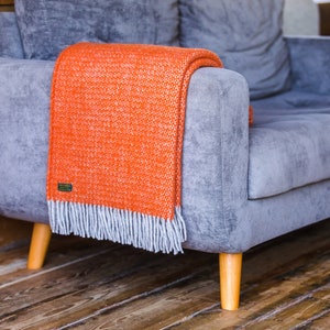 May include: A grey sofa with wooden legs and a bright orange throw blanket with a fringe.