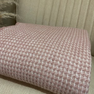 May include: A soft, pink and white waffle weave throw blanket. The blanket is folded and placed on a light beige sofa.