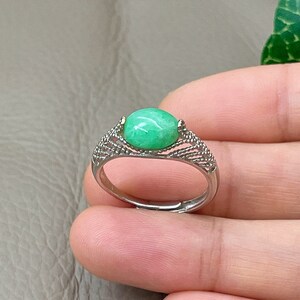 May include: A silver ring with a green oval gemstone set in a delicate, intricate design.