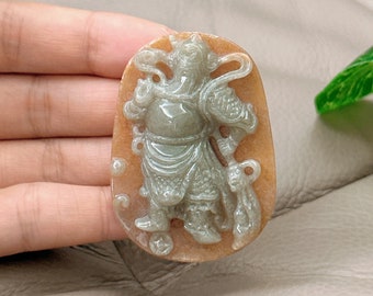 Op de afbeelding: Een jade hanger met een gedetailleerd gesneden figuur van een krijger, in lichtgroene kleur op een bruine achtergrond.