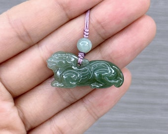 May include: A green jade pendant carved in the shape of a mythical creature, hanging from a pink cord with a green jade bead.