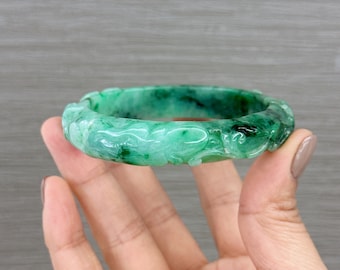 May include: A green jade bangle bracelet with intricate carvings. The bracelet is carved with a floral design and is a beautiful example of traditional Chinese craftsmanship.