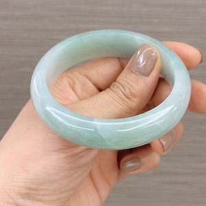 May include: A light green jade bangle bracelet. The bracelet is smooth and polished, with a subtle swirl pattern.