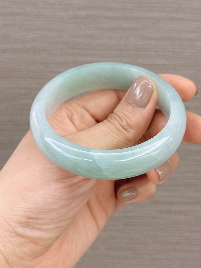 May include: A light green jade bangle bracelet. The bracelet is smooth and polished, with a subtle swirl pattern.