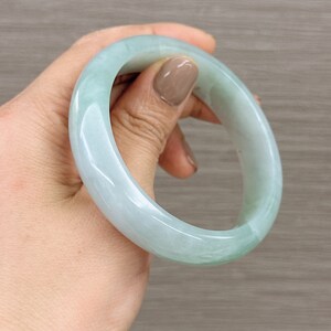 May include: A light green jade bangle bracelet. The bangle is smooth and polished, with a subtle swirl pattern.