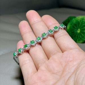 Op de afbeelding: Een zilveren armband met een rij ronde groene jade stenen gezet in een zilveren halo met kleinere heldere stenen.