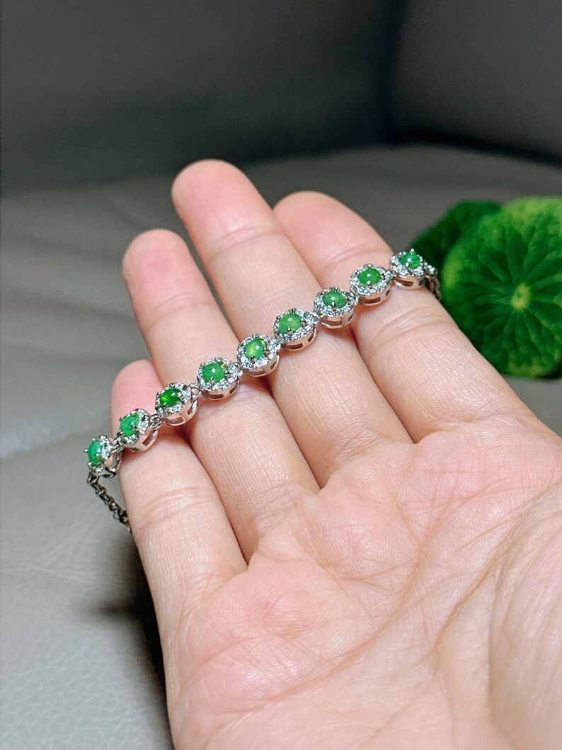 Op de afbeelding: Een zilveren armband met een rij ronde groene jade stenen gezet in een zilveren halo met kleinere heldere stenen.