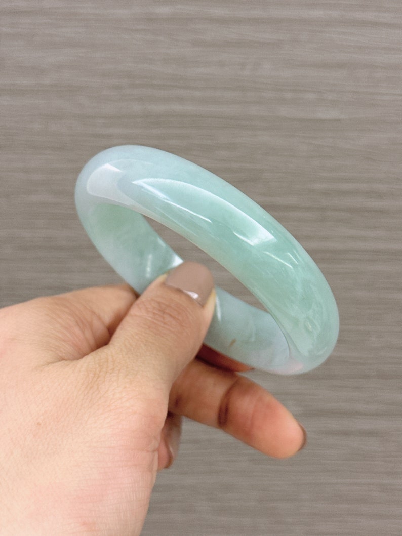 May include: A light green jade bangle bracelet. The bangle is smooth and polished, with a slightly translucent appearance.