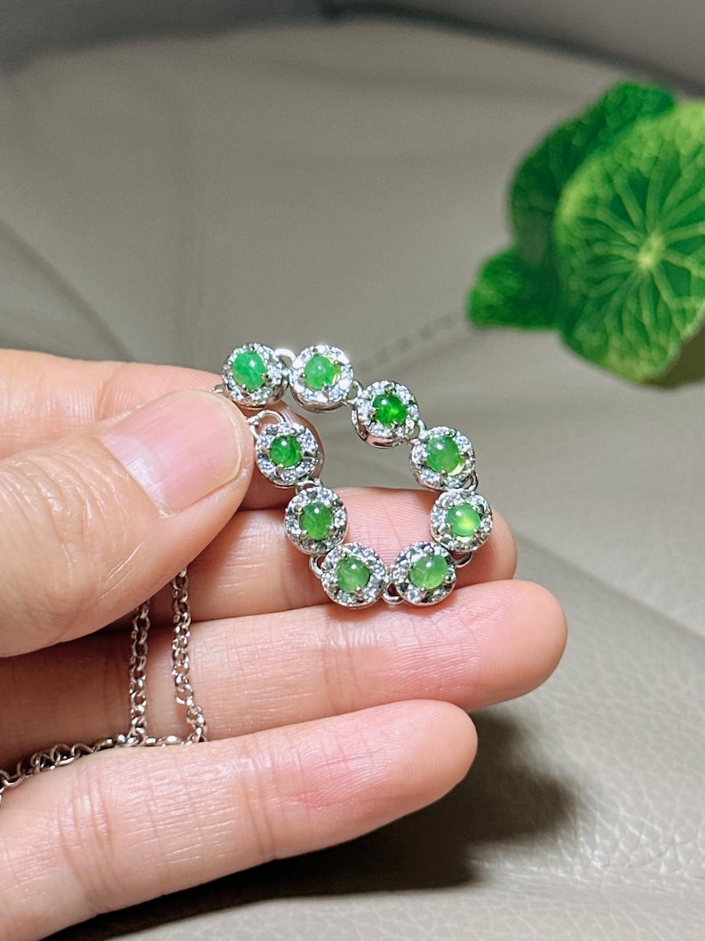 Op de afbeelding: Een zilveren ketting met een hanger met een cirkel van groene jade stenen omringd door kleinere heldere stenen.