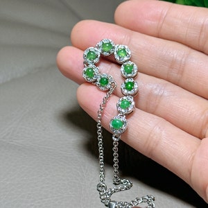 Op de afbeelding: Een zilveren armband met een ketting en een rij groene jade stenen gezet in zilver met kleine diamanten rond elke steen.