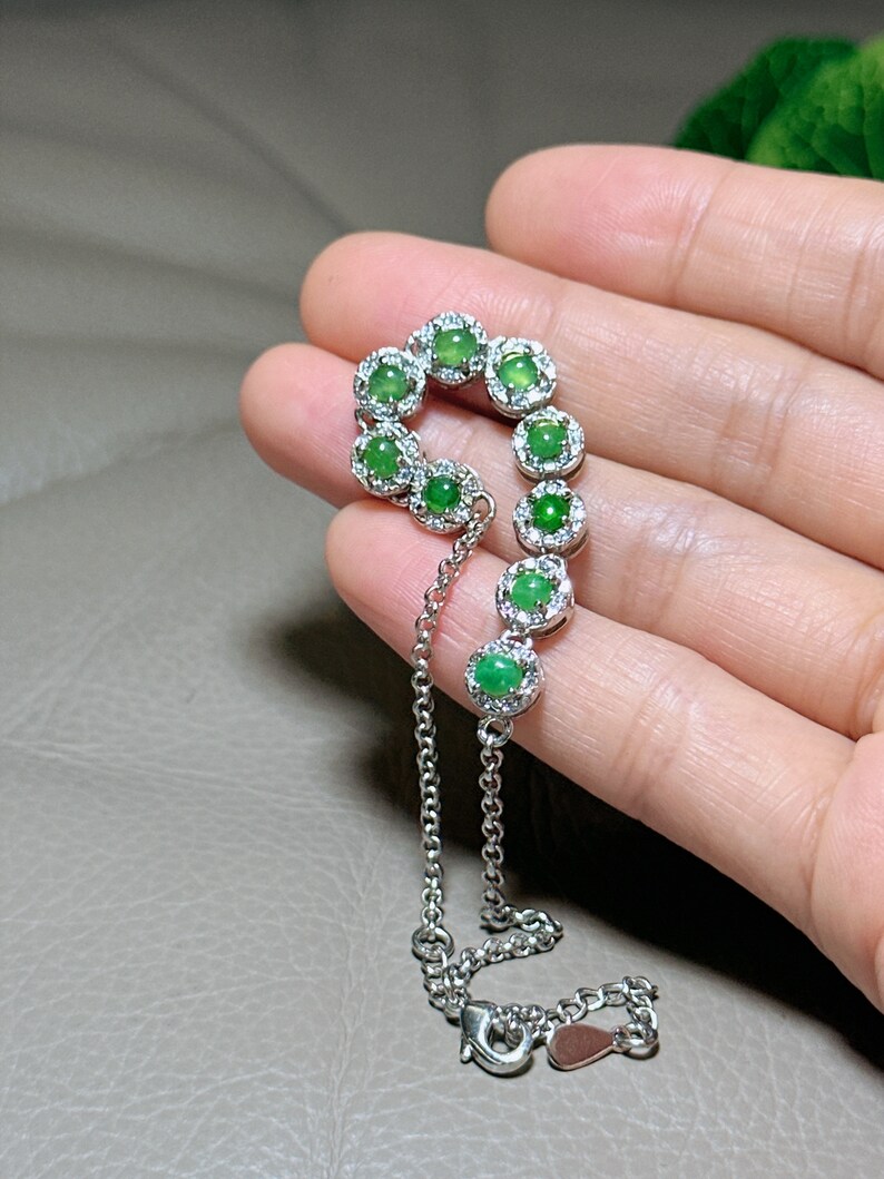 Op de afbeelding: Een zilveren armband met een ketting en een rij groene jade stenen gezet in zilver met kleine diamanten rond elke steen.