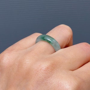 May include: A jade green ring with a smooth, polished finish. The ring is worn on a finger.