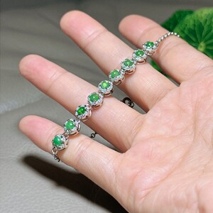 Op de afbeelding: Een zilveren armband met een ketting en zeven groene jade stenen gezet in zilver met kleine diamanten rond elke steen.