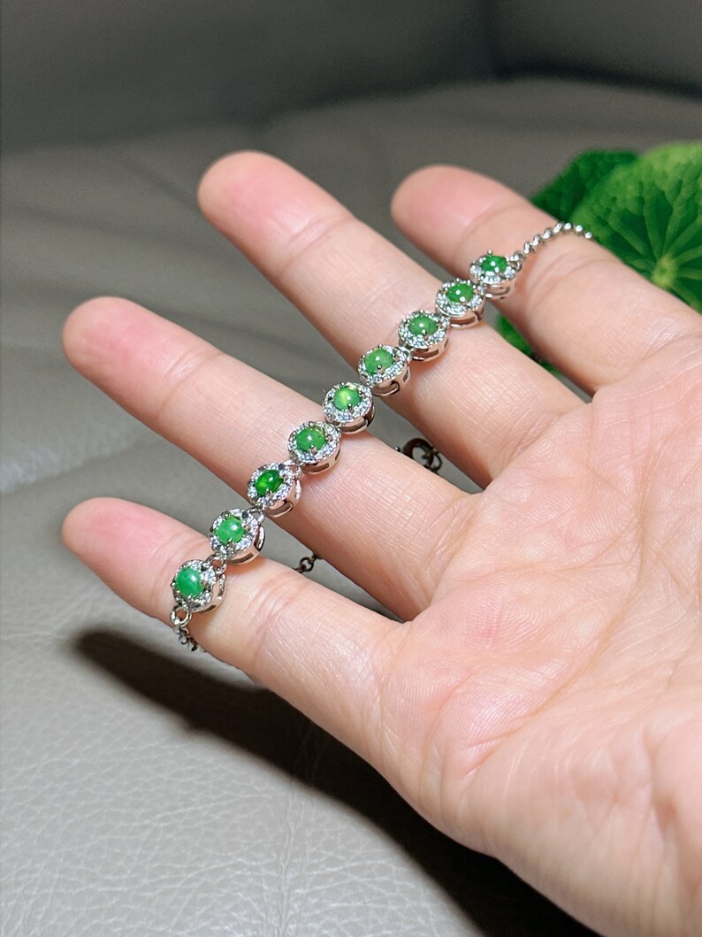 Op de afbeelding: Een zilveren armband met een ketting en zeven groene jade stenen gezet in zilver met kleine diamanten rond elke steen.