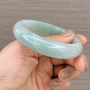 May include: A light green jade bangle bracelet. The bangle is smooth and polished, with a subtle swirl pattern.