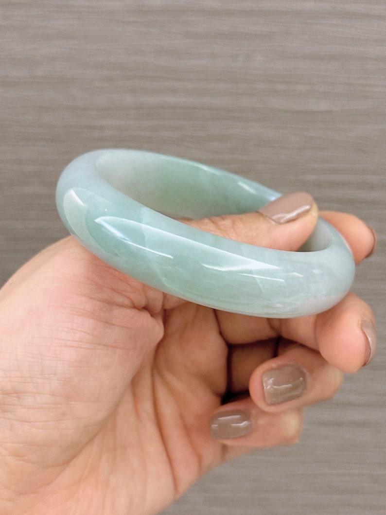 May include: A light green jade bangle bracelet. The bangle is smooth and polished, with a subtle swirl pattern.