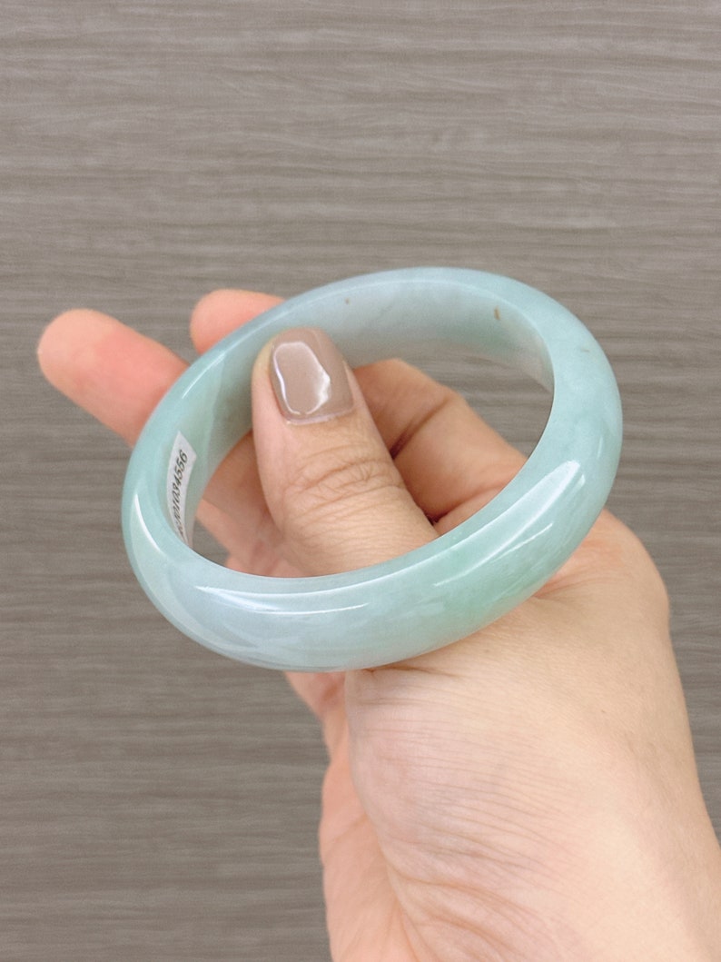 May include: A light green jade bangle bracelet. The bracelet is smooth and polished.
