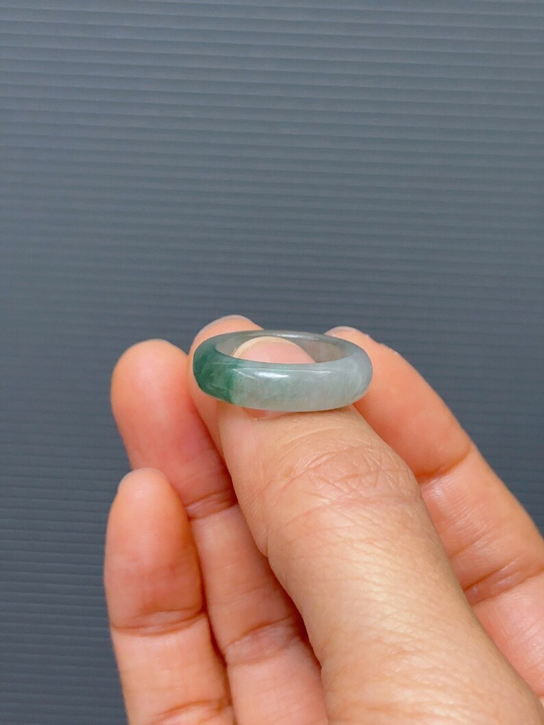 May include: A jade ring with a light green and white color gradient. The ring is made of natural jade and has a smooth, polished finish.