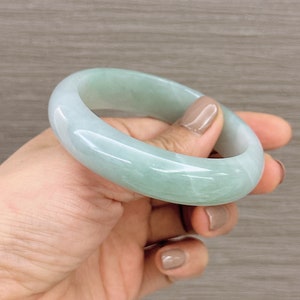 May include: A light green jade bangle bracelet. The bangle is smooth and polished, with a subtle marbled pattern.