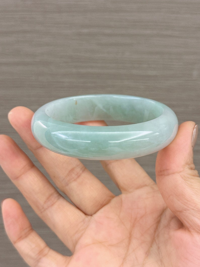May include: A light green jade bangle bracelet. The bracelet is smooth and polished, with a slightly oval shape.