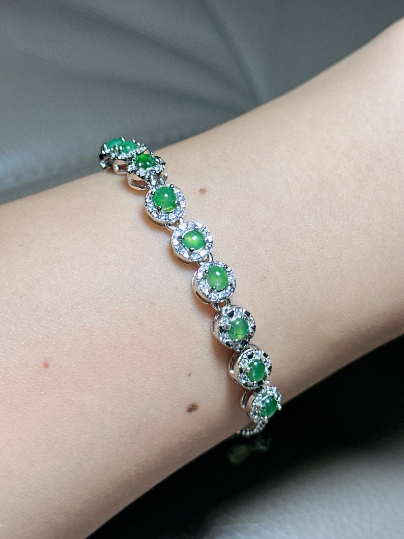 Op de afbeelding: Een zilveren armband met groene jade stenen en een halo-setting van diamanten.